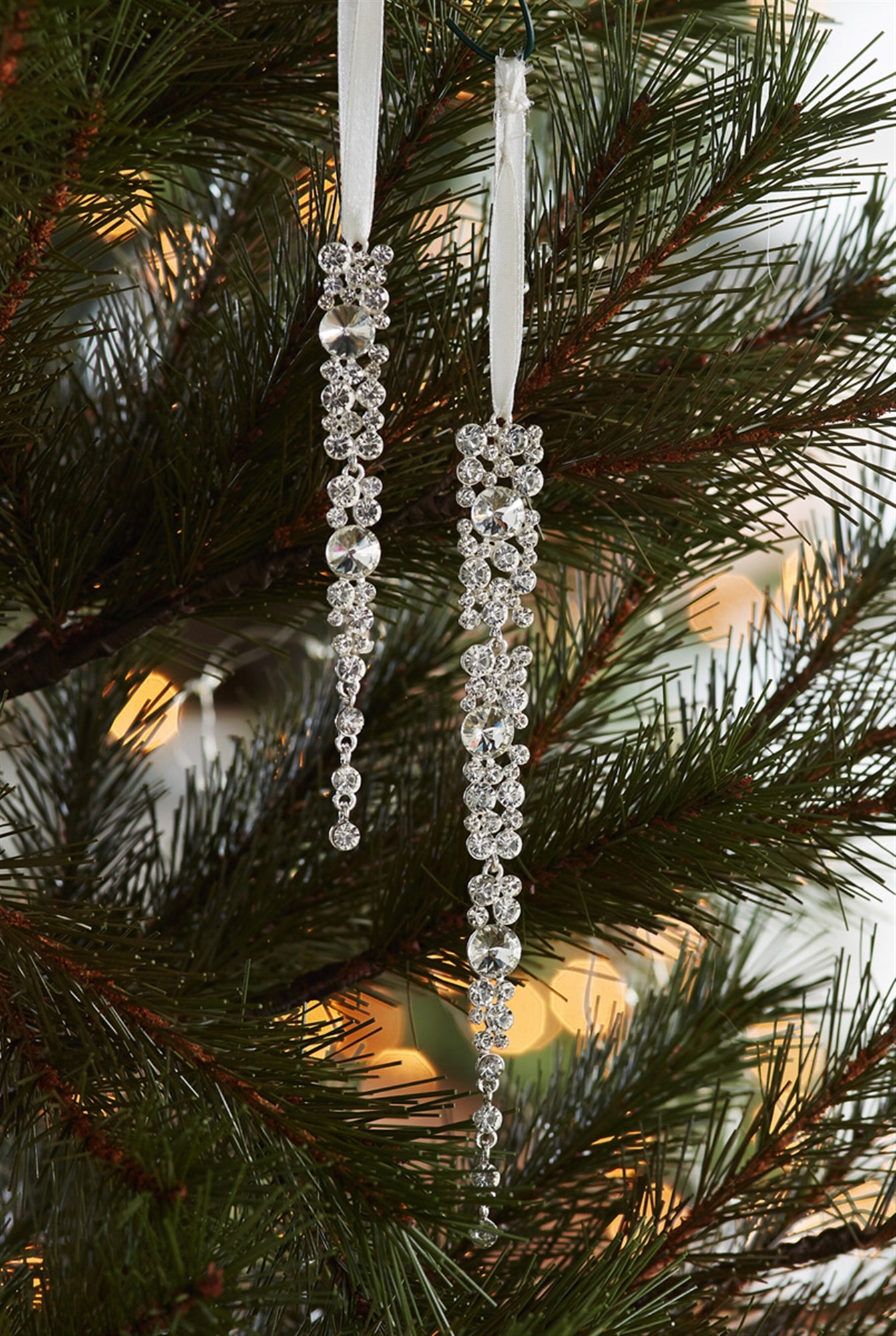 A pair of modern jeweled icicle ornaments hanging on a Christmas tree, sparkling against the warm glow of the lights.