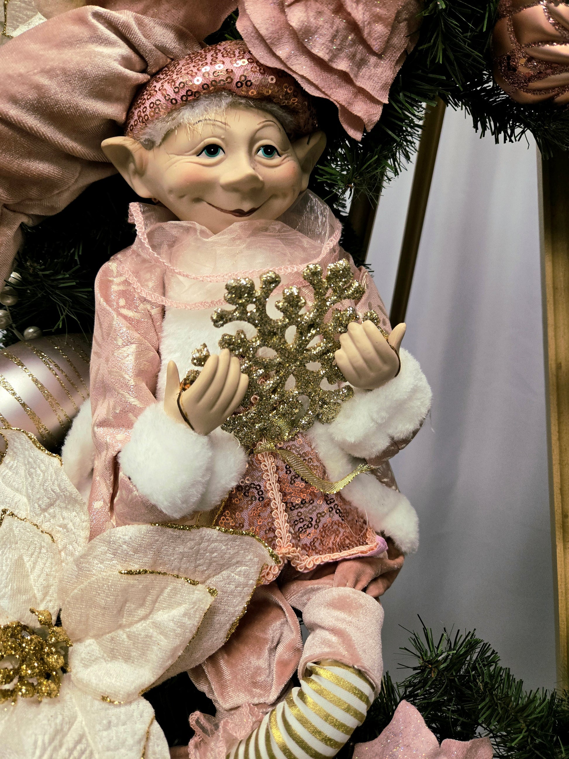 22″ Christmas wreath in pink, cream & gold featuring an elf figure, poinsettias, ornament balls, gold picks, and a multi-ribbon bow
