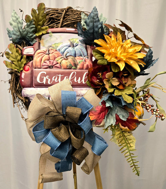 12″ grapevine wreath with metal truck sign saying “Grateful,” fall florals, greenery, pumpkin/berry pick, and large brown-blue burlap bow
