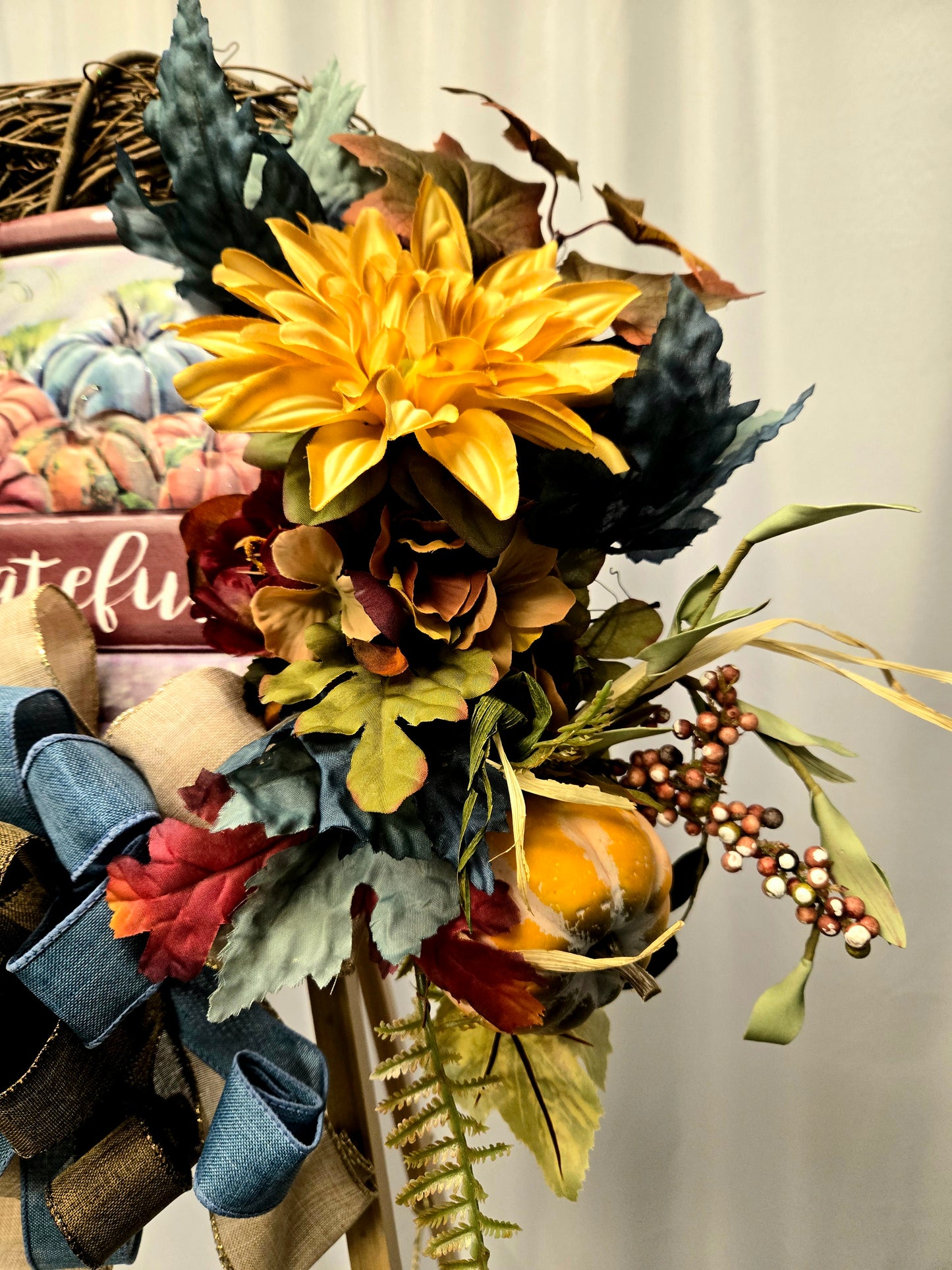 12″ grapevine wreath with metal truck sign saying “Grateful,” fall florals, greenery, pumpkin/berry pick, and large brown-blue burlap bow
