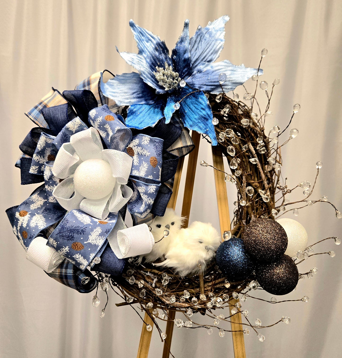 12″ grapevine wreath with two snowy white owls, ornamental balls, crystal picks, blue poinsettia, and multi-ribbon bow
